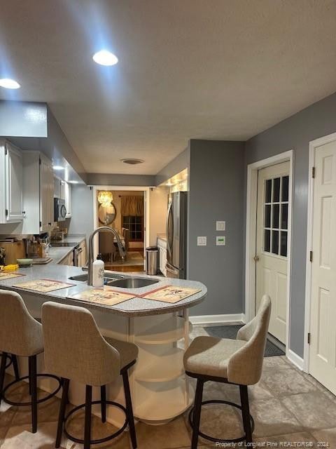 kitchen featuring a kitchen bar, baseboards, a sink, a peninsula, and appliances with stainless steel finishes