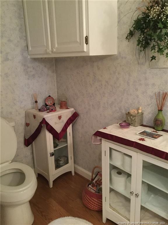 half bathroom featuring baseboards, wallpapered walls, toilet, and wood finished floors