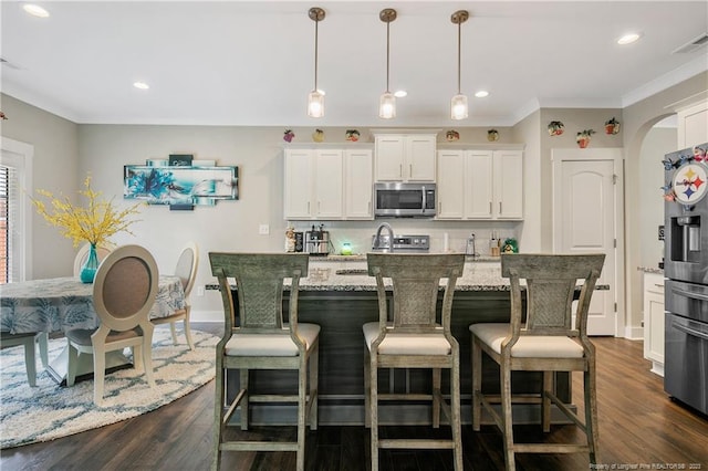 kitchen with hanging light fixtures, light stone counters, stainless steel appliances, dark hardwood / wood-style flooring, and a kitchen island with sink