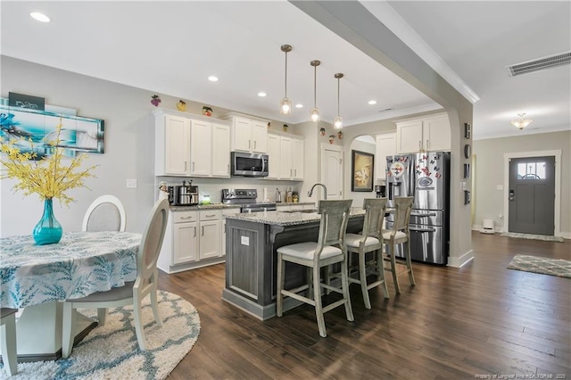 kitchen with hanging light fixtures, appliances with stainless steel finishes, an island with sink, light stone counters, and dark hardwood / wood-style flooring