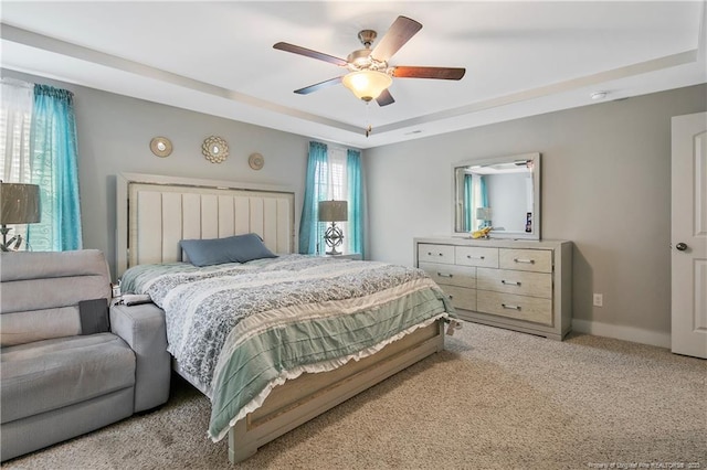 carpeted bedroom with ceiling fan and a tray ceiling