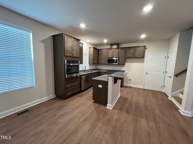 kitchen featuring dark brown cabinetry, a kitchen breakfast bar, appliances with stainless steel finishes, a kitchen island, and hardwood / wood-style flooring