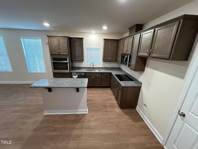 kitchen with wood-type flooring, sink, appliances with stainless steel finishes, a kitchen island, and dark brown cabinetry