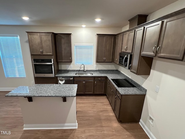 kitchen featuring light stone countertops, sink, stainless steel appliances, a kitchen breakfast bar, and light hardwood / wood-style flooring