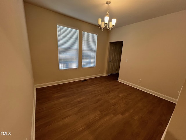 unfurnished room featuring dark wood-type flooring and an inviting chandelier