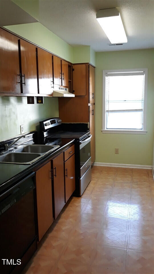 kitchen with black dishwasher, dark countertops, stainless steel electric range oven, under cabinet range hood, and a sink