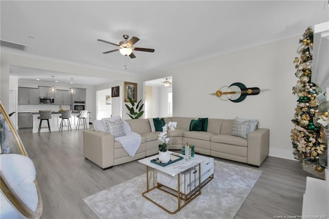 living room featuring ornamental molding, light hardwood / wood-style flooring, and ceiling fan