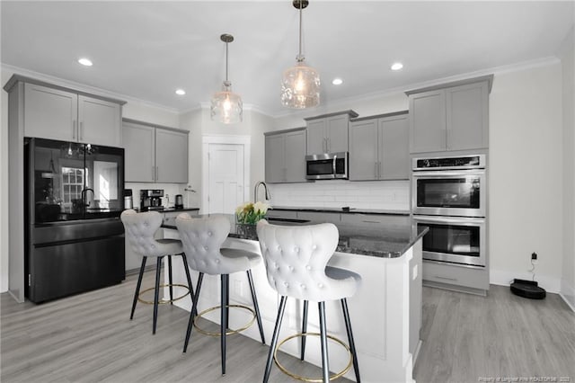 kitchen featuring an island with sink, hanging light fixtures, gray cabinetry, stainless steel appliances, and a breakfast bar