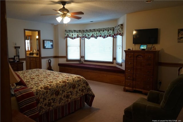 bedroom with ceiling fan, connected bathroom, light colored carpet, and a textured ceiling