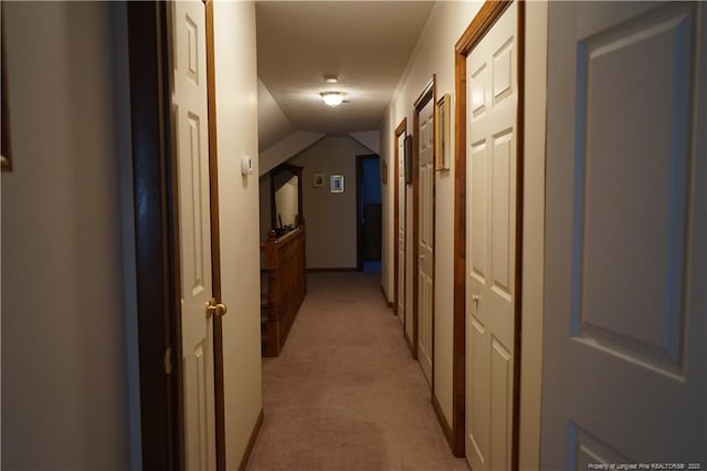 corridor featuring vaulted ceiling and light colored carpet