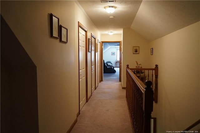 hallway featuring lofted ceiling, light colored carpet, and a textured ceiling