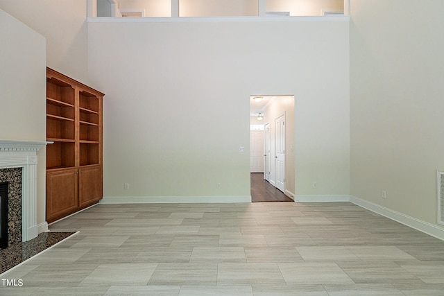 unfurnished living room with a high end fireplace, light tile patterned floors, and a high ceiling