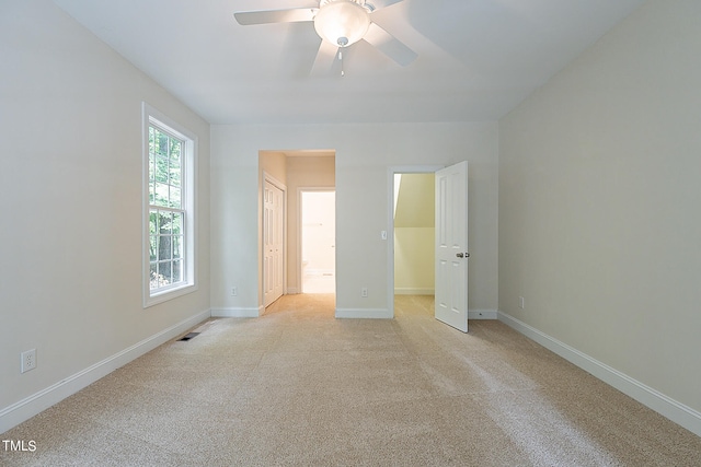 unfurnished bedroom with ceiling fan, ensuite bath, light colored carpet, and multiple windows