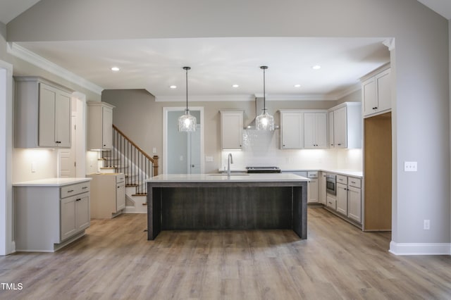 kitchen with light wood-type flooring, sink, pendant lighting, stainless steel microwave, and an island with sink