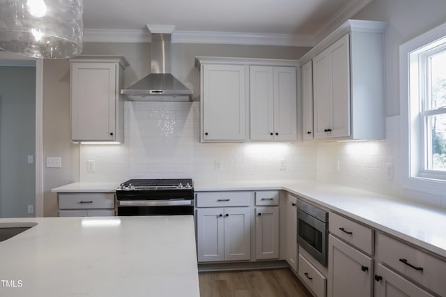 kitchen featuring stainless steel appliances, white cabinetry, a healthy amount of sunlight, and wall chimney range hood