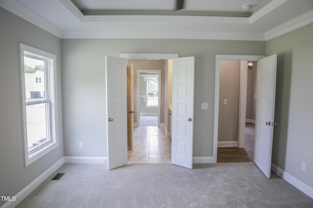 unfurnished bedroom featuring a raised ceiling, multiple windows, light colored carpet, and ornamental molding