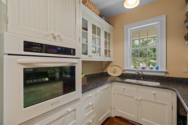 kitchen with stainless steel oven, white cabinetry, dark stone countertops, and sink