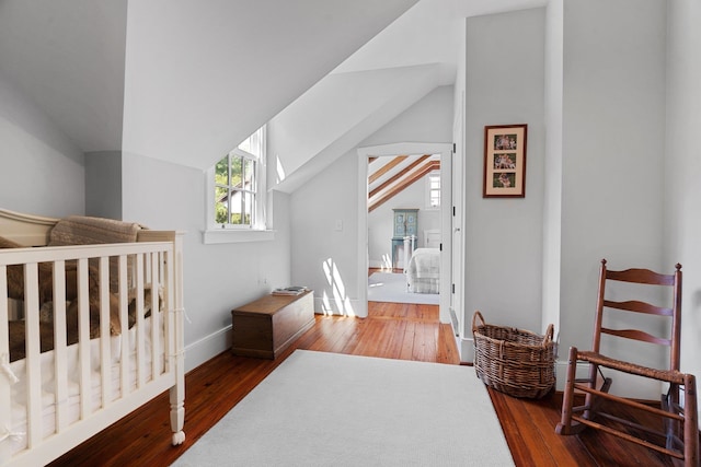 bedroom with a nursery area, hardwood / wood-style flooring, and lofted ceiling