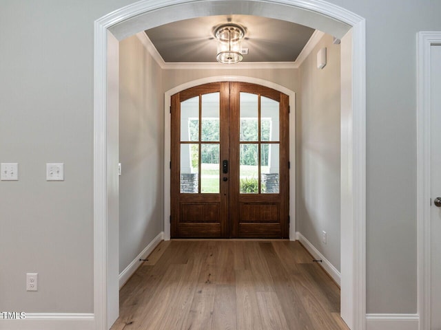 entryway featuring crown molding, an inviting chandelier, light hardwood / wood-style flooring, and french doors