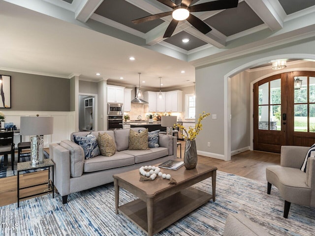 living room featuring light hardwood / wood-style floors, beamed ceiling, coffered ceiling, ornamental molding, and ceiling fan