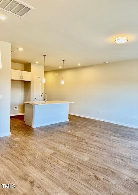 kitchen featuring white cabinets, light hardwood / wood-style flooring, hanging light fixtures, and an island with sink