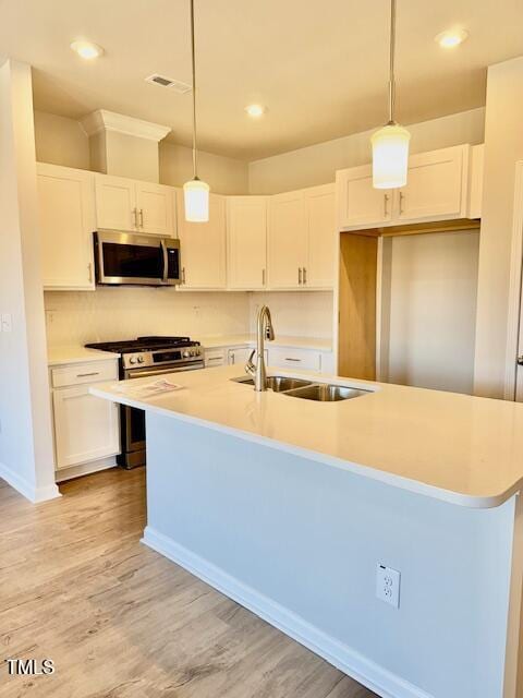 kitchen featuring appliances with stainless steel finishes, decorative light fixtures, white cabinetry, and a center island with sink