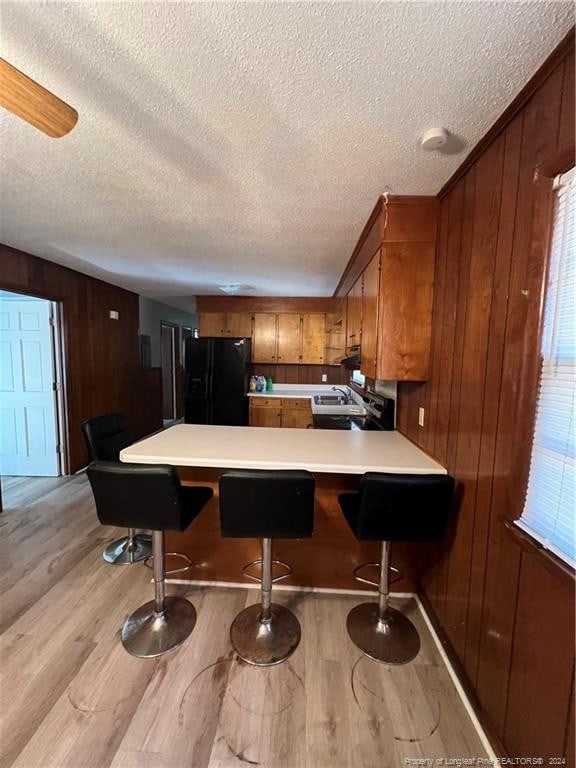 kitchen featuring a textured ceiling, light hardwood / wood-style flooring, black fridge, and kitchen peninsula