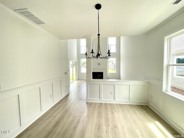 unfurnished dining area with visible vents, a decorative wall, an inviting chandelier, ornamental molding, and light wood-type flooring