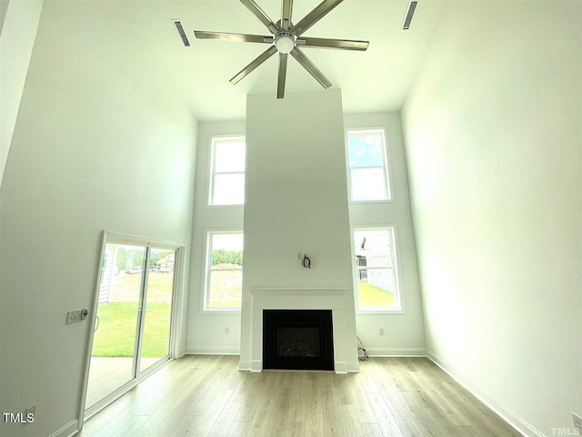 unfurnished living room with visible vents, a towering ceiling, light wood-style floors, a fireplace, and a wealth of natural light