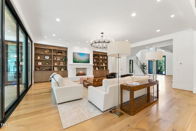 living room with an inviting chandelier, built in shelves, and light wood-type flooring