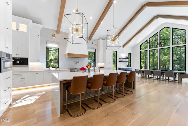 kitchen featuring beam ceiling, a breakfast bar, stainless steel oven, light hardwood / wood-style flooring, and white cabinetry