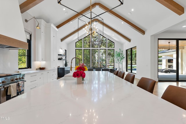 kitchen with light stone countertops, white cabinetry, a notable chandelier, beam ceiling, and high end stainless steel range