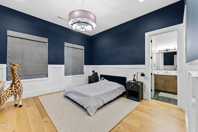 bedroom with light hardwood / wood-style floors, connected bathroom, and a notable chandelier