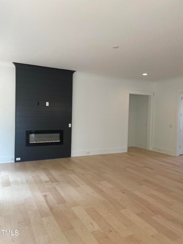 interior space featuring a large fireplace, ornamental molding, and light hardwood / wood-style flooring