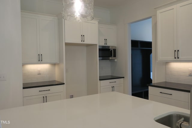 kitchen featuring decorative backsplash, white cabinets, and hanging light fixtures