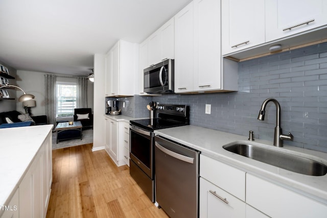 kitchen featuring sink, tasteful backsplash, appliances with stainless steel finishes, white cabinets, and light wood-type flooring