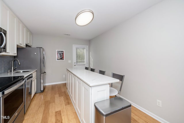 kitchen featuring white cabinets, light hardwood / wood-style flooring, appliances with stainless steel finishes, tasteful backsplash, and a kitchen island