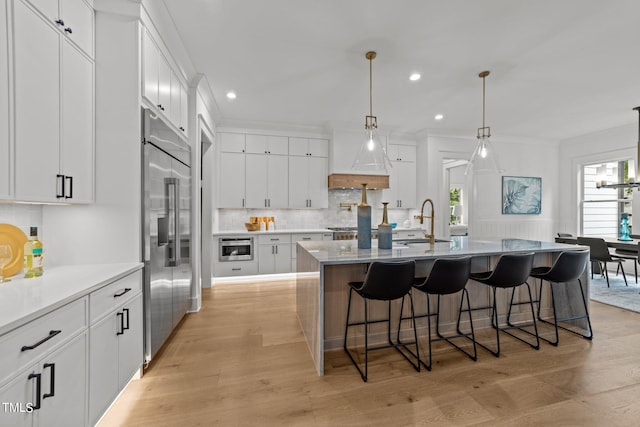 kitchen with light wood-type flooring, sink, an island with sink, white cabinetry, and stainless steel built in fridge