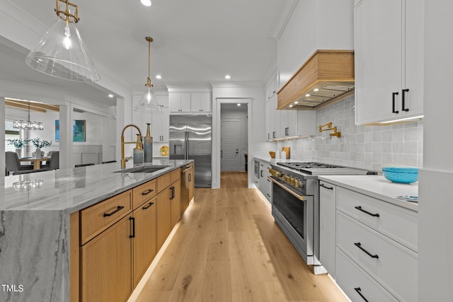 kitchen featuring light stone counters, white cabinets, sink, high end appliances, and light hardwood / wood-style flooring