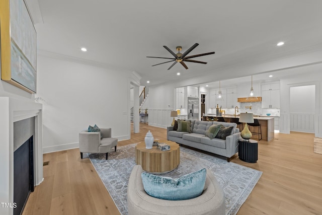 living room with ceiling fan, ornamental molding, light hardwood / wood-style floors, and a high end fireplace