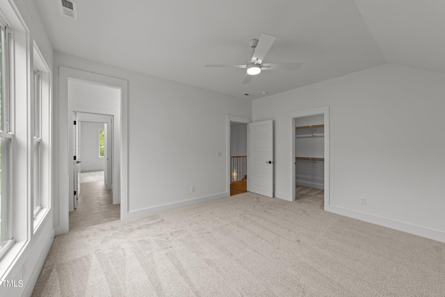 unfurnished bedroom featuring light carpet, vaulted ceiling, a spacious closet, and ceiling fan