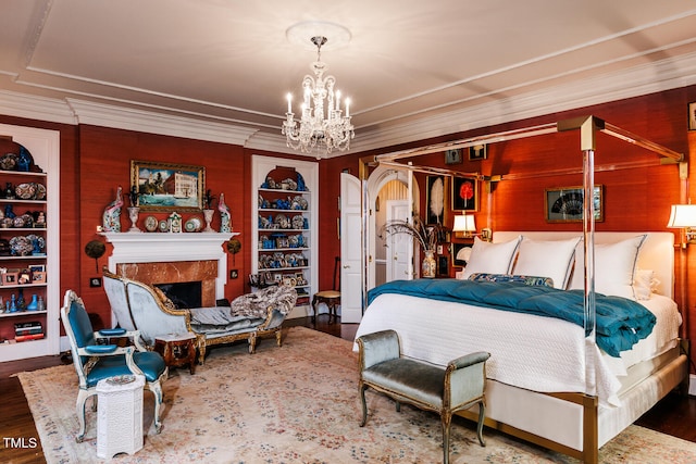 bedroom with an inviting chandelier, wooden walls, a fireplace, dark hardwood / wood-style flooring, and ornamental molding