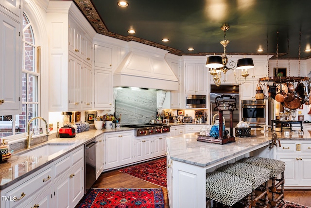 kitchen with premium range hood, decorative light fixtures, sink, built in appliances, and light stone countertops