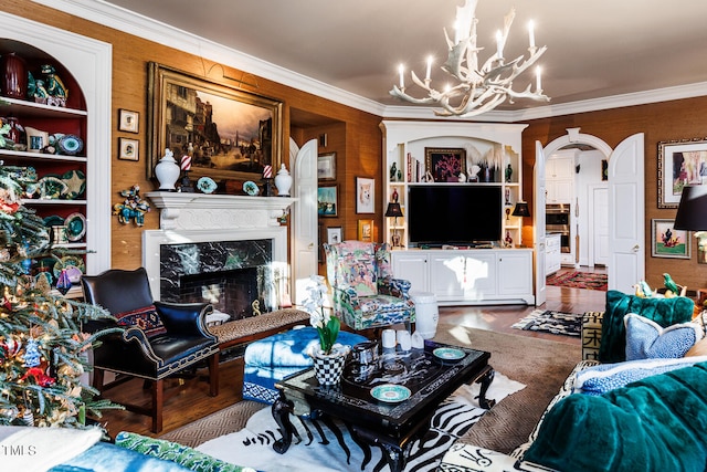 living room featuring built in shelves, a premium fireplace, ornamental molding, a notable chandelier, and hardwood / wood-style flooring