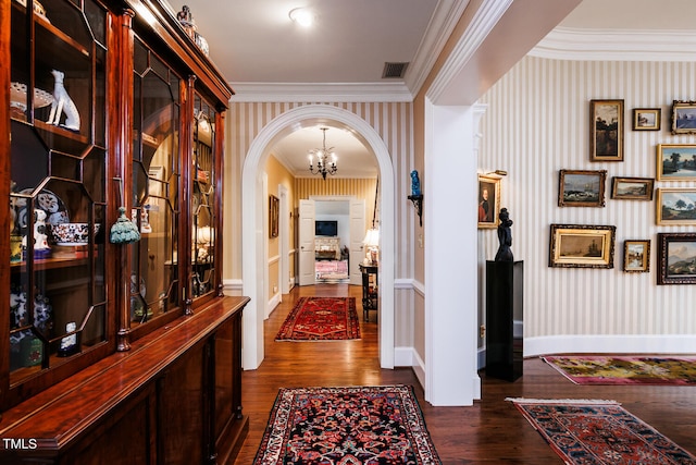 corridor with an inviting chandelier, ornamental molding, and dark wood-type flooring