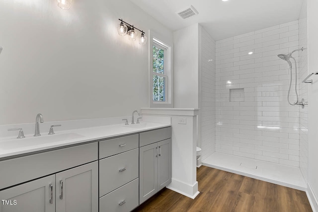 bathroom with wood-type flooring, vanity, toilet, and tiled shower