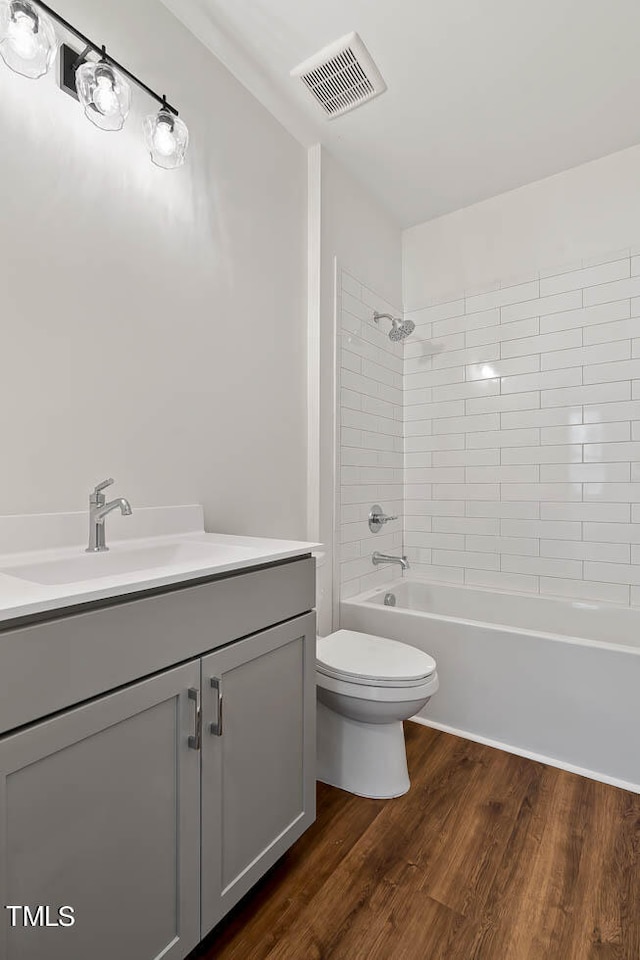 full bathroom featuring wood-type flooring, vanity, tiled shower / bath combo, and toilet