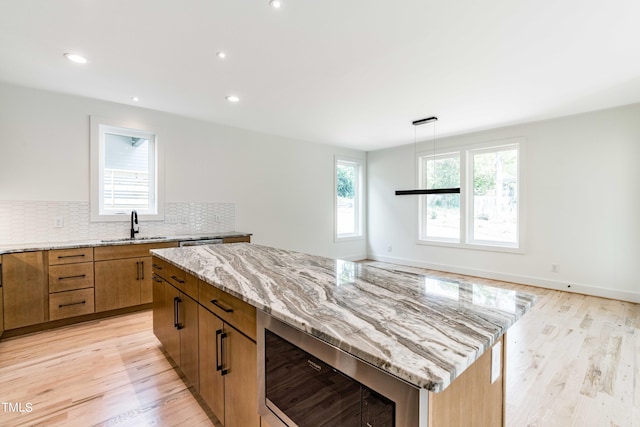 kitchen with light stone counters, hanging light fixtures, light hardwood / wood-style floors, tasteful backsplash, and a center island