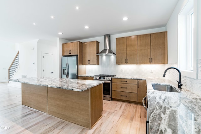 kitchen featuring appliances with stainless steel finishes, tasteful backsplash, light wood-type flooring, wall chimney exhaust hood, and sink