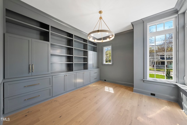 empty room featuring a notable chandelier, built in features, light wood-type flooring, and ornamental molding